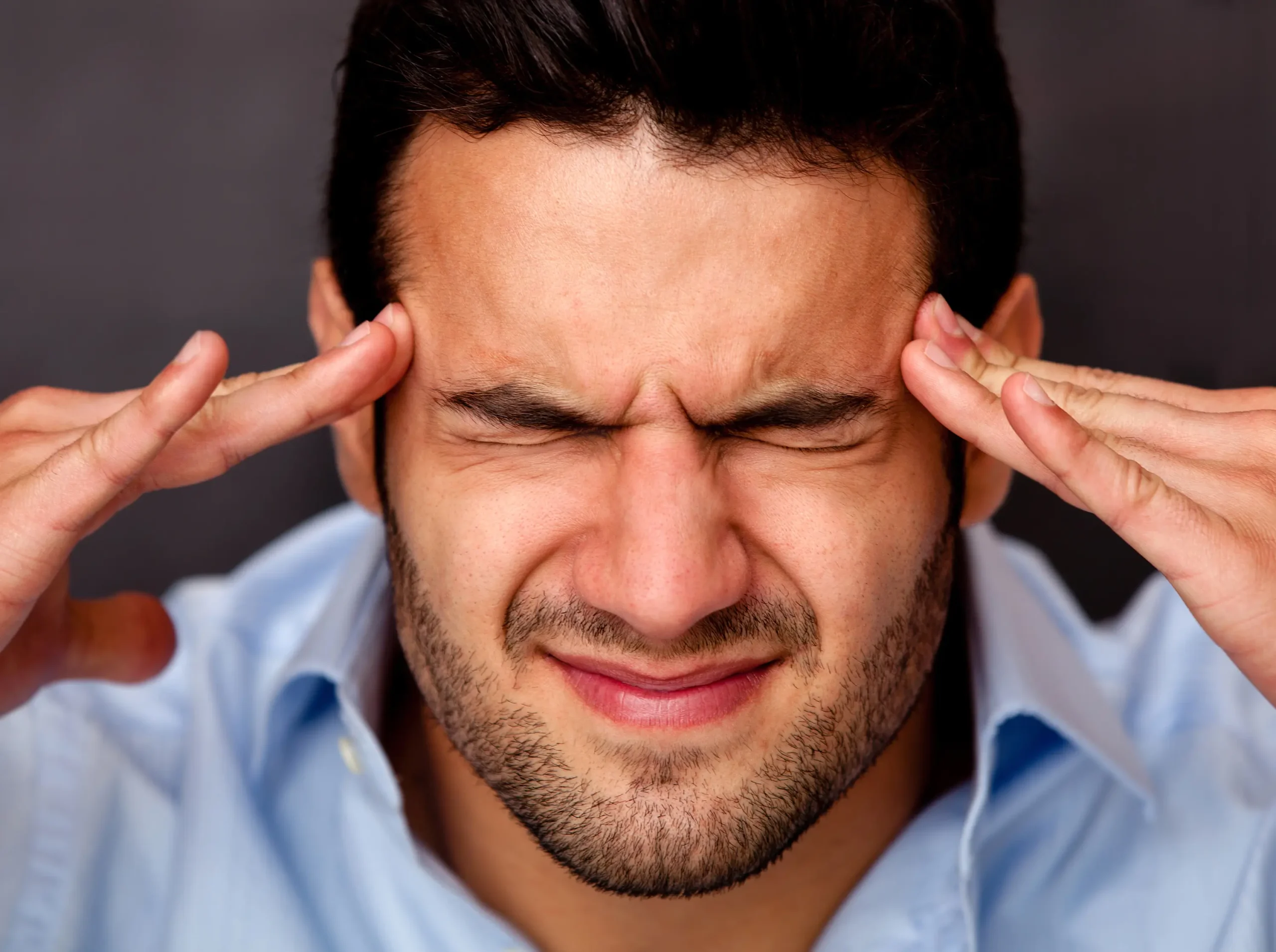 Man holding his temples in pain, suffering from a headache or migraine, seeking relief through remedial massage.